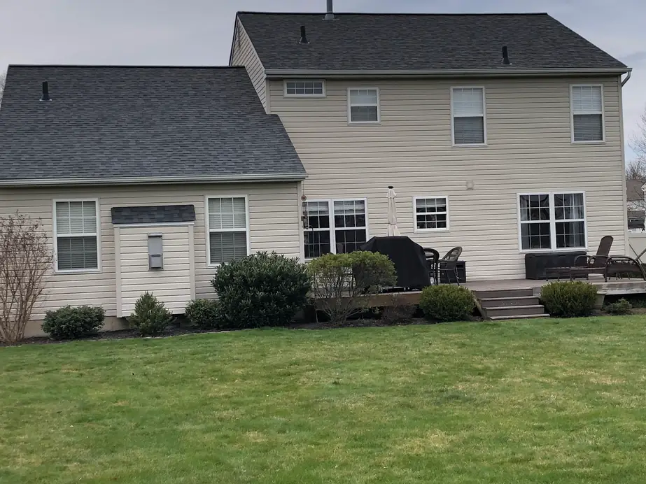 Rear elevation of a home with a new roof, tan vinyl siding, capped trim and a deck, completed by Aronson Roofing and Siding